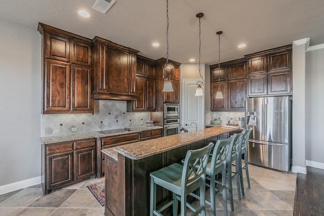 kitchen featuring light stone countertops, appliances with stainless steel finishes, pendant lighting, and a center island with sink