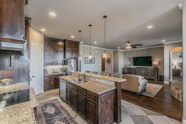 kitchen featuring stainless steel appliances, dark brown cabinets, ornamental molding, arched walkways, and ceiling fan