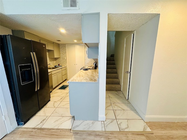 kitchen featuring tasteful backsplash, sink, a textured ceiling, and black refrigerator with ice dispenser