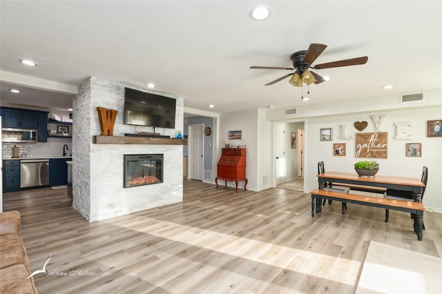 living room featuring ceiling fan, a fireplace, sink, and light hardwood / wood-style flooring