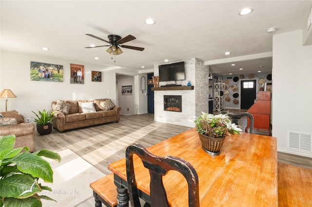 living room with wood-type flooring, a large fireplace, and ceiling fan