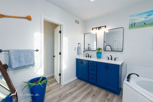 bathroom with hardwood / wood-style flooring, vanity, and tiled bath