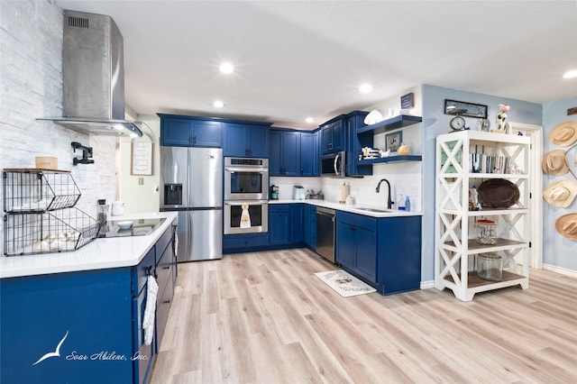 kitchen with sink, blue cabinetry, appliances with stainless steel finishes, wall chimney exhaust hood, and light wood-type flooring