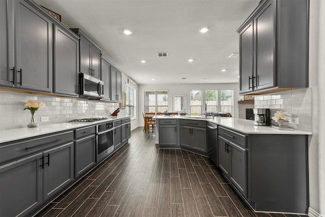 kitchen with appliances with stainless steel finishes, tasteful backsplash, sink, gray cabinetry, and kitchen peninsula