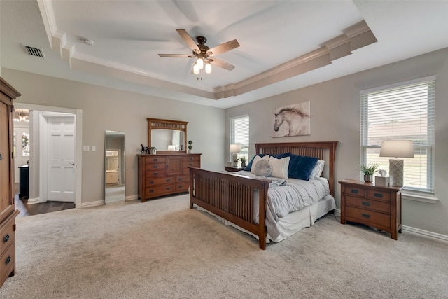 carpeted bedroom with a raised ceiling, ornamental molding, ceiling fan, and ensuite bath