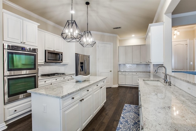 kitchen featuring stainless steel appliances, white cabinets, light stone counters, and decorative light fixtures