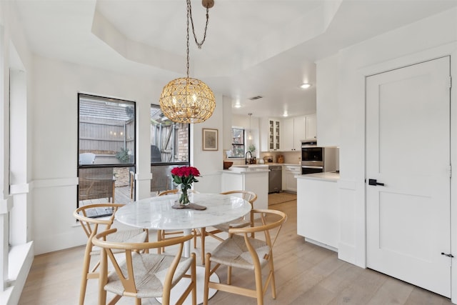 dining area featuring a chandelier, a raised ceiling, sink, and light wood-type flooring