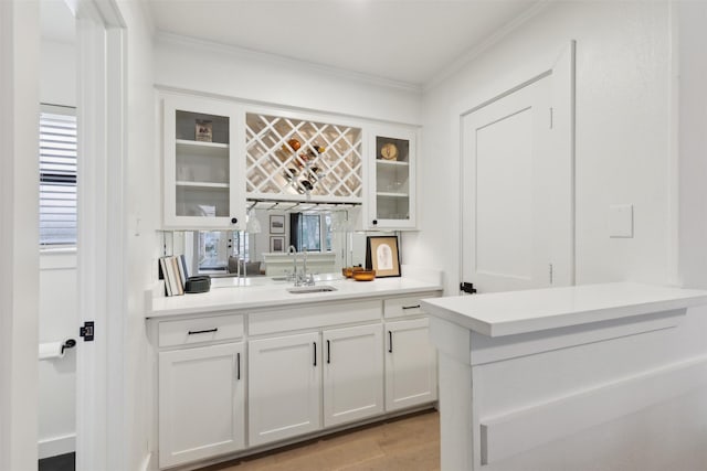 bar featuring crown molding, light wood-type flooring, sink, and white cabinets