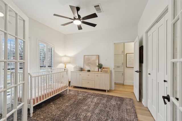 bedroom with ceiling fan, light hardwood / wood-style floors, a closet, and a crib