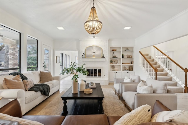 living room with crown molding, built in features, a notable chandelier, light hardwood / wood-style floors, and a brick fireplace