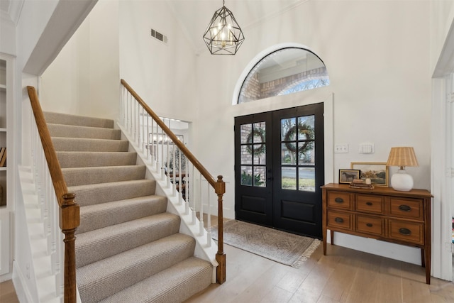 entryway with an inviting chandelier, a towering ceiling, french doors, and light wood-type flooring