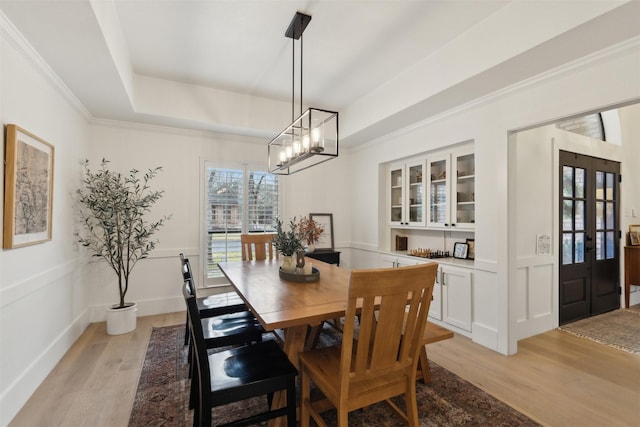 dining room featuring crown molding, a tray ceiling, french doors, and light wood-type flooring