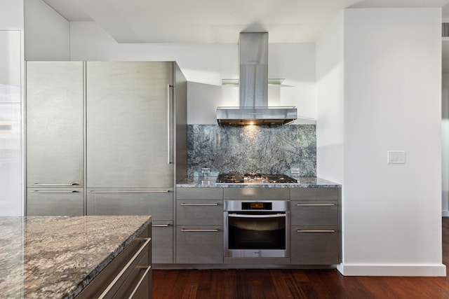 kitchen featuring island exhaust hood, appliances with stainless steel finishes, dark hardwood / wood-style floors, and dark stone countertops