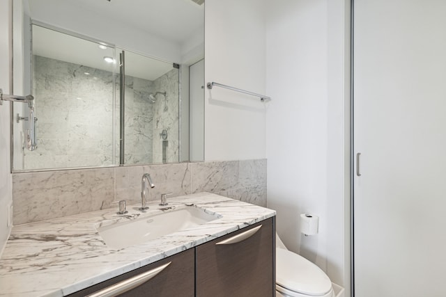 bathroom with vanity, tiled shower, toilet, and decorative backsplash