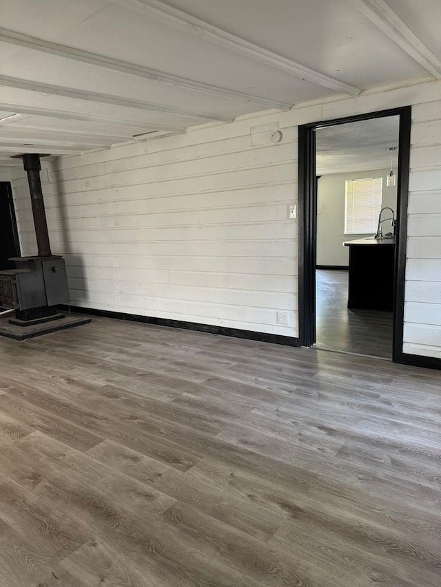 unfurnished living room with wood-type flooring, a wood stove, wooden walls, and beam ceiling