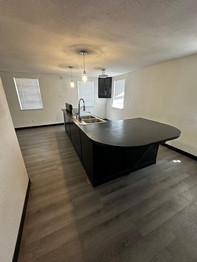 kitchen featuring dark hardwood / wood-style floors, decorative light fixtures, sink, a center island, and a textured ceiling