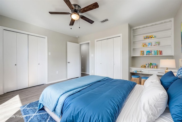 bedroom with visible vents, light wood-style flooring, multiple closets, and ceiling fan