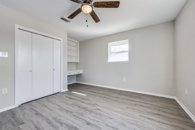 unfurnished bedroom with ceiling fan, a closet, built in desk, and light hardwood / wood-style flooring