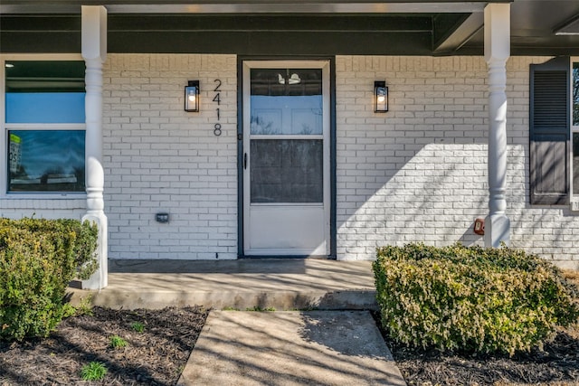 view of exterior entry featuring brick siding and covered porch