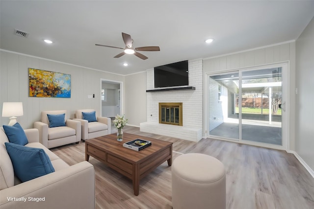 living room with crown molding, ceiling fan, a fireplace, and light hardwood / wood-style floors