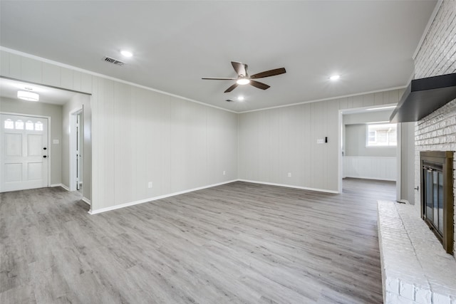 unfurnished living room with visible vents, wood finished floors, a brick fireplace, and ornamental molding