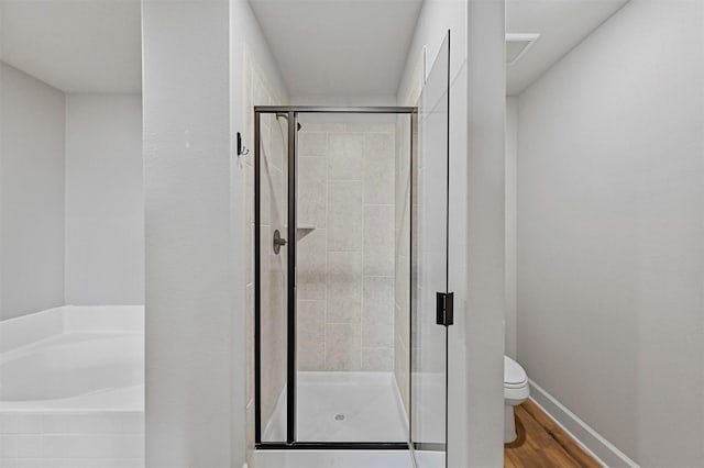 bathroom with toilet, hardwood / wood-style floors, and shower with separate bathtub