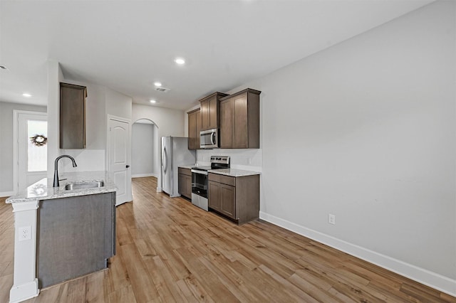 kitchen with sink, light hardwood / wood-style flooring, stainless steel appliances, dark brown cabinetry, and light stone countertops