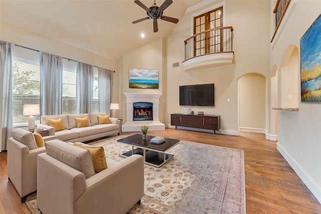 living room featuring a fireplace with raised hearth, high vaulted ceiling, wood finished floors, and baseboards