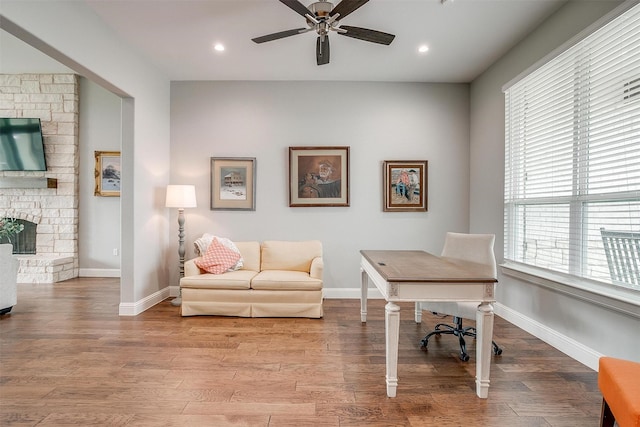 office space featuring ceiling fan, a stone fireplace, and light hardwood / wood-style flooring