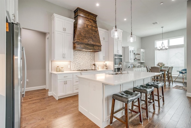 kitchen with white cabinetry, decorative light fixtures, a center island with sink, a kitchen breakfast bar, and stainless steel appliances