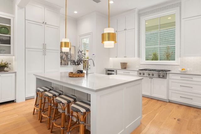 kitchen with stainless steel gas stovetop, an island with sink, pendant lighting, and white cabinets