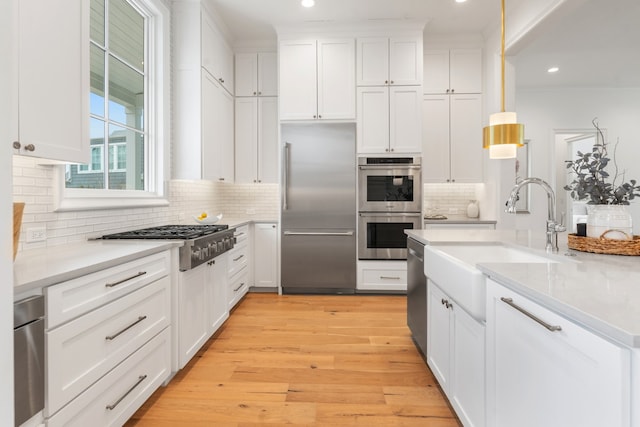 kitchen with pendant lighting, sink, appliances with stainless steel finishes, white cabinets, and light wood-type flooring