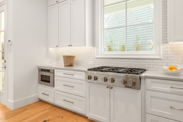 kitchen with white cabinetry, stainless steel gas cooktop, light hardwood / wood-style flooring, and backsplash