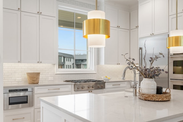 kitchen with sink, hanging light fixtures, appliances with stainless steel finishes, light stone countertops, and white cabinets