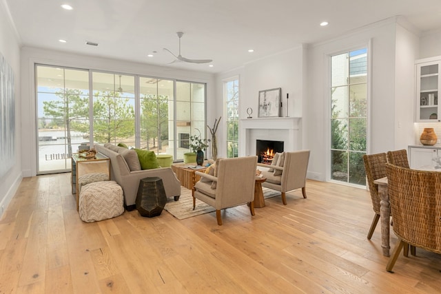 living area with ornamental molding, ceiling fan, and light wood-type flooring