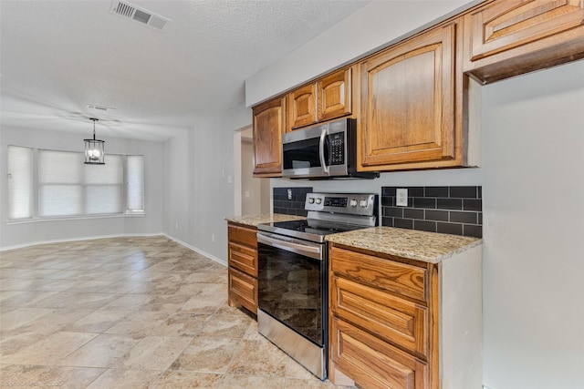 kitchen featuring appliances with stainless steel finishes, tasteful backsplash, light stone countertops, a textured ceiling, and decorative light fixtures