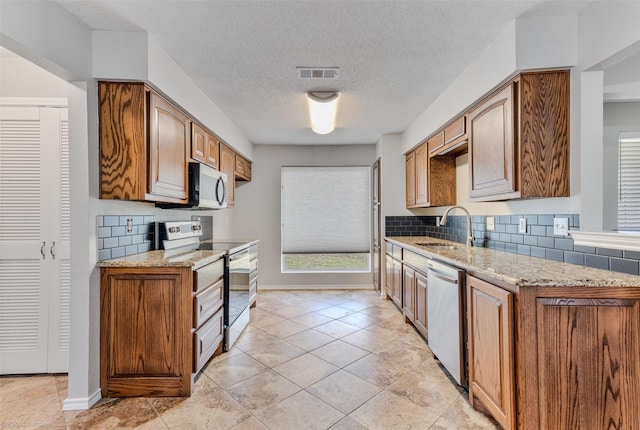 kitchen with stainless steel appliances, light stone countertops, sink, and decorative backsplash