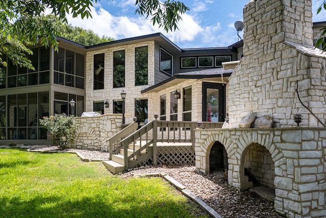 rear view of property featuring stone siding, a chimney, and a sunroom