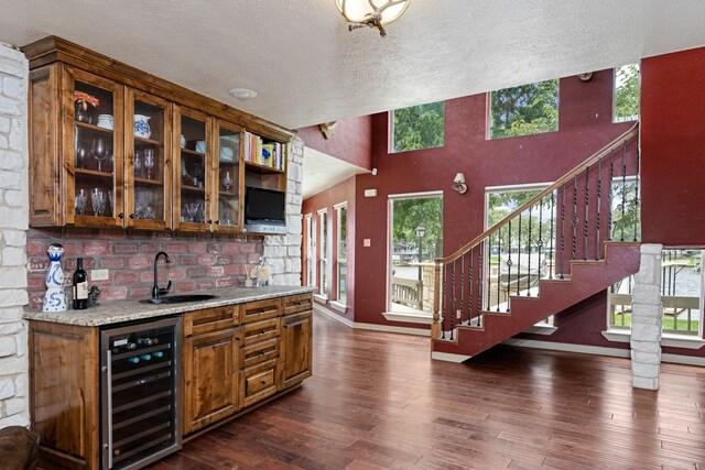 bar featuring sink, dark hardwood / wood-style floors, light stone counters, a textured ceiling, and beverage cooler