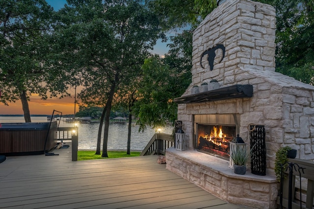 deck at dusk with a water view and an outdoor stone fireplace