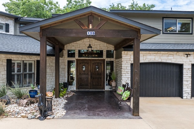 view of exterior entry with a garage, concrete driveway, a shingled roof, and stone siding