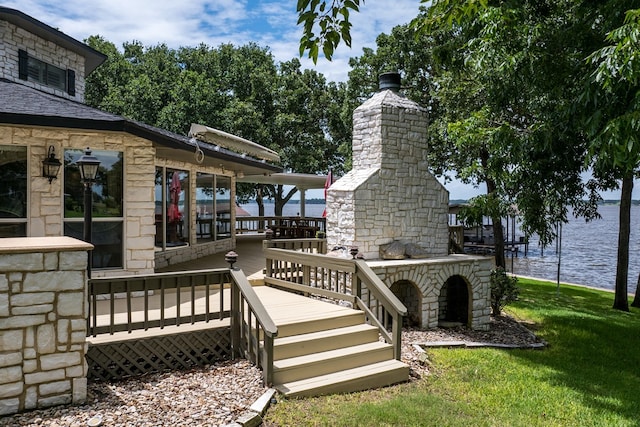 wooden deck featuring a water view, a stone fireplace, and a lawn