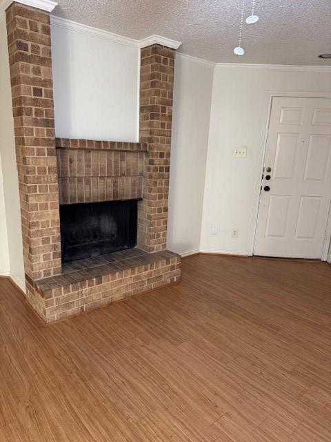 unfurnished living room with ornamental molding, a brick fireplace, hardwood / wood-style floors, and a textured ceiling