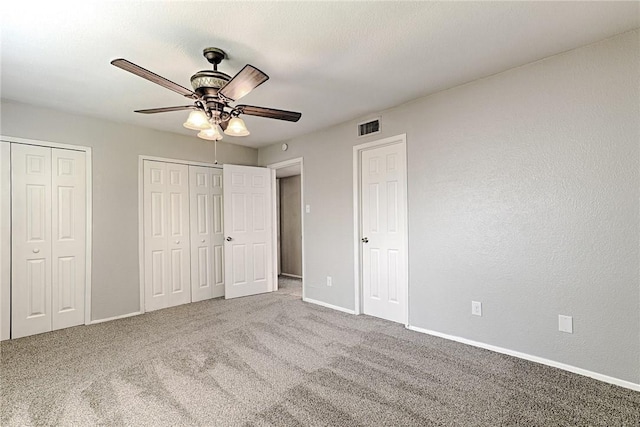 unfurnished bedroom with ceiling fan, multiple closets, and carpet flooring