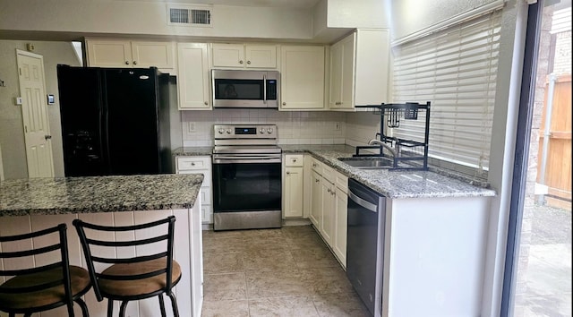 kitchen with sink, appliances with stainless steel finishes, a kitchen breakfast bar, light stone countertops, and backsplash