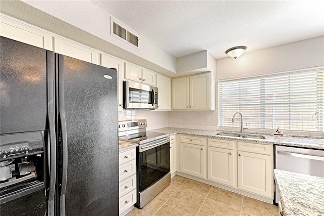 kitchen with sink, a textured ceiling, light tile patterned floors, appliances with stainless steel finishes, and light stone countertops