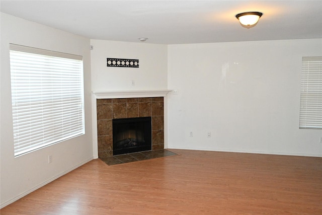 unfurnished living room with a tiled fireplace and wood-type flooring