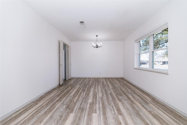 spare room featuring a chandelier and light wood-type flooring