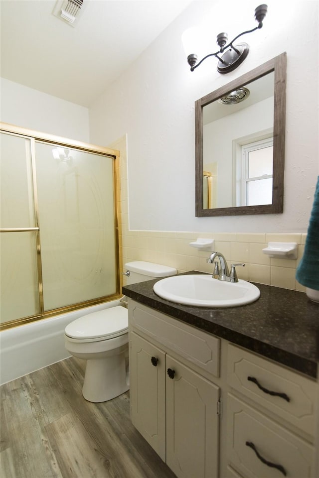 full bathroom with shower / bath combination with glass door, tile walls, vanity, wood-type flooring, and toilet