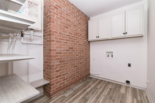 clothes washing area featuring cabinets, hookup for a washing machine, electric dryer hookup, hardwood / wood-style flooring, and brick wall